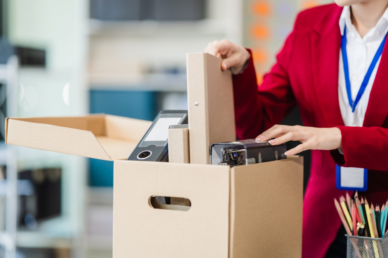 Professional worker in red suit packs a box full of her office belongings.